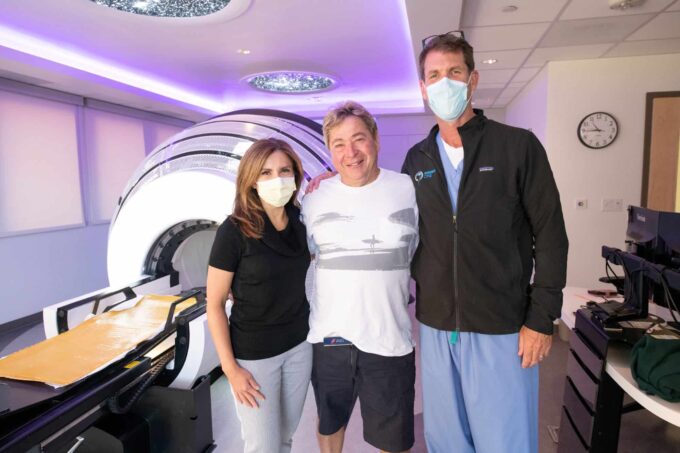 Patient Bill Lawson poses between two physicians at Neurosurgery One. The ZAP-X radiosurgery machine in the background