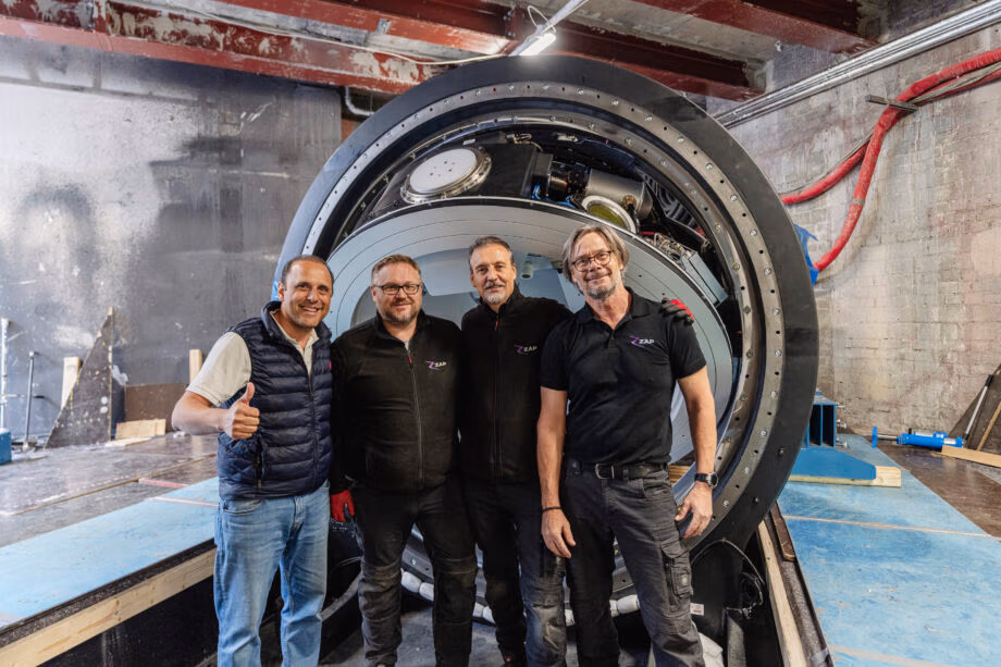 A team of engineers stands proudly in front of the ZAP-X® Gyroscopic Radiosurgery system, an advanced, self-shielded radiosurgery platform designed for non-invasive brain tumor treatment. The image captures the innovative spirit behind ZAP Surgical Systems, showcasing the precision engineering and teamwork that drive the development of cutting-edge stereotactic radiosurgery (SRS) technology.