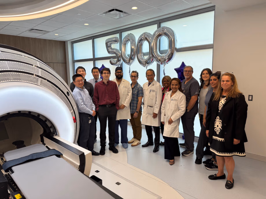Christopher Czerwinski, the 5,000th patient treated with the ZAP-X® Gyroscopic Radiosurgery® platform, stands with physicians, staff, and administrators at Jersey Shore University Medical Center. The group is gathered beside the ZAP-X system with silver “5000” balloons marking the occasion