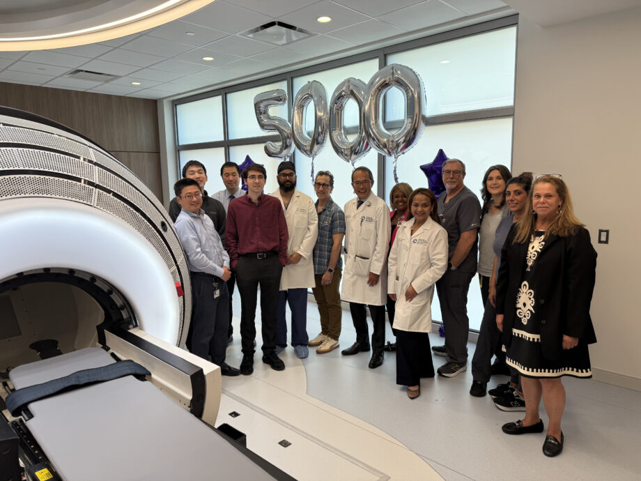 Christopher Czerwinski, the 5,000th patient treated with the ZAP-X® Gyroscopic Radiosurgery® platform, stands with physicians, staff, and administrators at Jersey Shore University Medical Center. The group is gathered beside the ZAP-X system with silver “5000” balloons marking the occasion