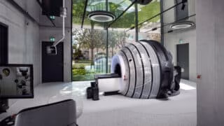ZAP-X installation in modern room with concrete floor and mirrored ceiling. A floor-to-ceiling glass wall is behind the machine