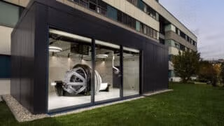 Modern black steel building addition with floor-to-ceiling glass windows showing ZAP-X installation inside