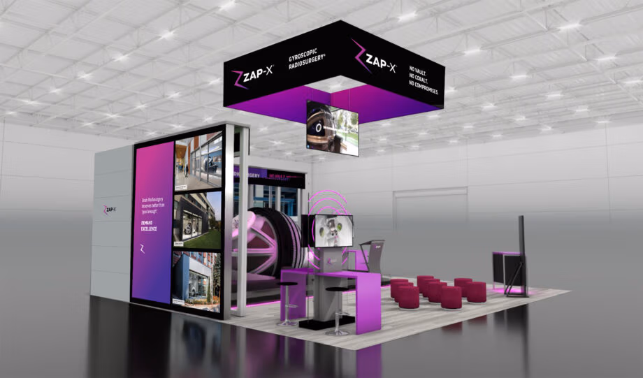 Exhibit booth for ZAP Surgical at ASTRO 2025 showcasing the debut of the ZAP-X® Gyroscopic Radiosurgery® system. The booth features bold black and purple branding with illuminated signage reading “No Vault. No Cobalt. No Compromises.” A suspended overhead cube displays the ZAP-X logo, while large digital screens present video demonstrations and clinical images. At the center, a display of the ZAP-X treatment system is highlighted with purple lighting accents. The booth includes a reception counter with monitors, seating for attendees, and modern architectural panels featuring the tagline “Brain Radiosurgery deserves better than ‘good enough.’ DEMAND EXCELLENCE.”