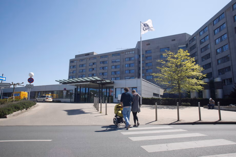 Alfried Krupp Hospital in Essen, Germany, featuring the main entrance of the modern medical facility with people walking across a crosswalk on a sunny day.