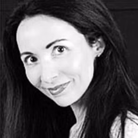 A close-up, black-and-white portrait of ZAP-X patient Yolanda. She has long dark hair cascading past her shoulders, large expressive eyes, and a warm smile. Yolanda’s head is tilted slightly to one side against a plain dark background, conveying a friendly, confident demeanor.