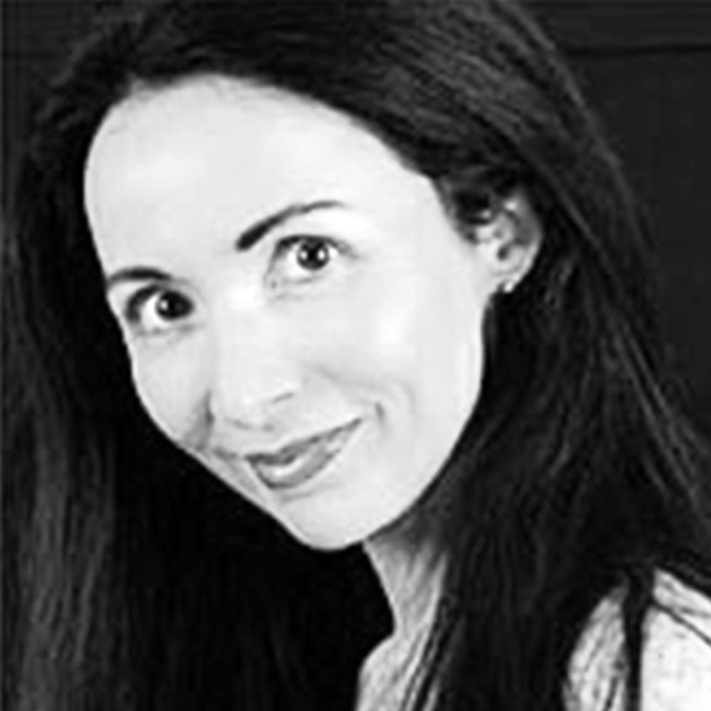 A close-up, black-and-white portrait of ZAP-X patient Yolanda. She has long dark hair cascading past her shoulders, large expressive eyes, and a warm smile. Yolanda’s head is tilted slightly to one side against a plain dark background, conveying a friendly, confident demeanor.